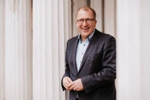 Torsten Bechtel Abgebildet ist Torsten Bechtel im blauen Anzug- Er lacht und hat die Hände zueinander gefaltet.